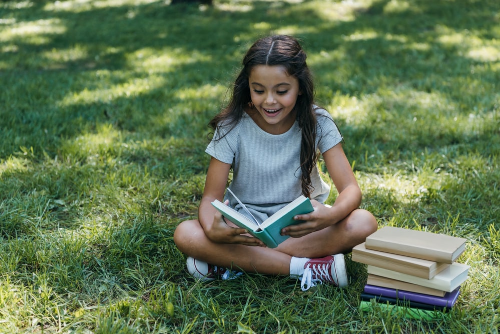 Student happily reading a book while sitting on green grass